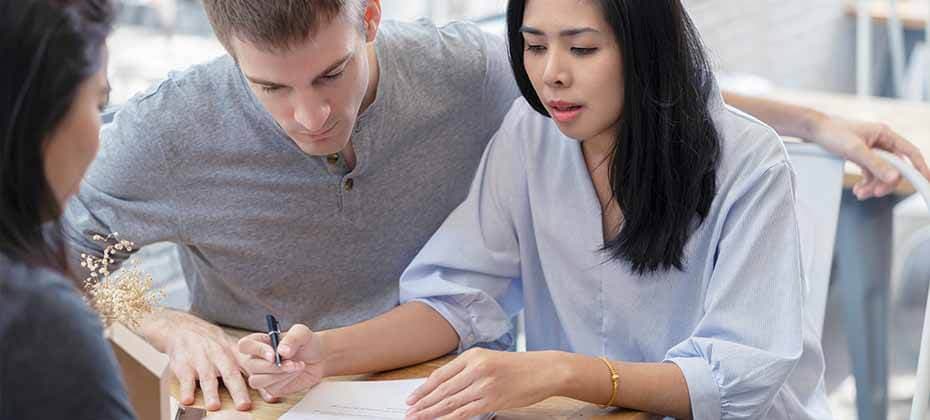 Three individuals reviewing financial documents at a table, with one person holding a pen