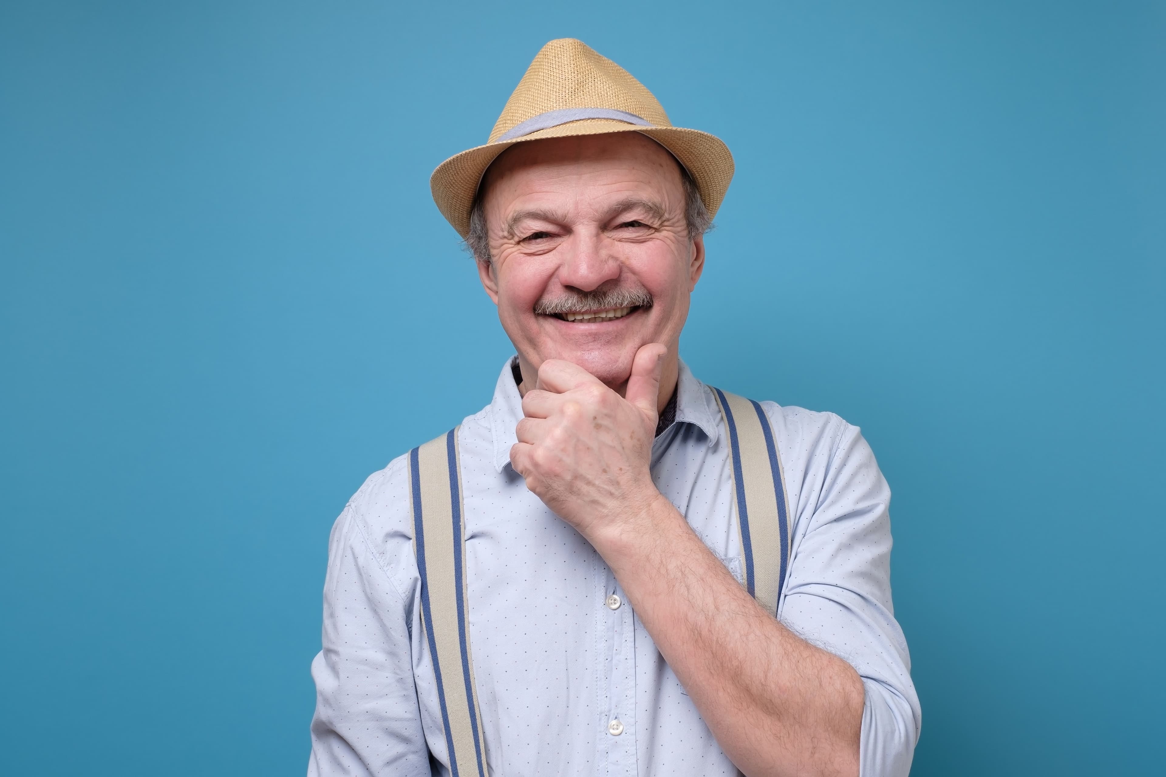 Person in suspenders and straw hat standing thoughtfully
