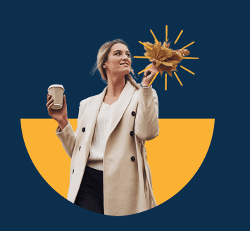 Lady wearing a coat holding a coffee cup in one hand and autumn leaf in the other