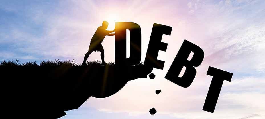 Silhouette of a person pushing the word DEBT off a cliff into sunlight symbolizing debt relief and financial freedom
