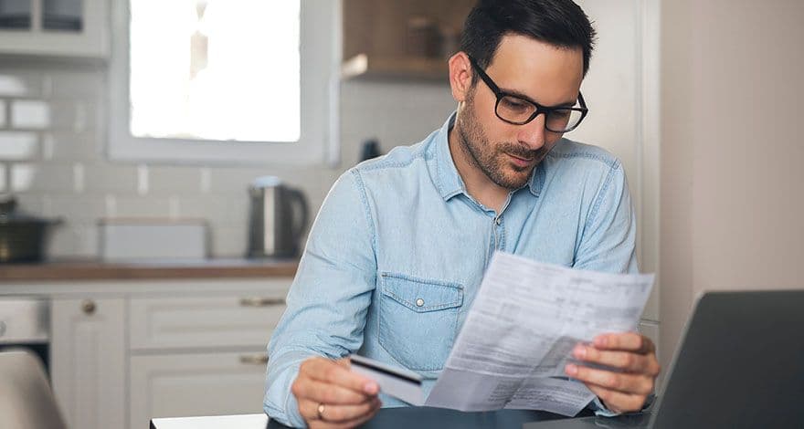 Person sitting at a kitchen table holding a piece of paper and a credit card