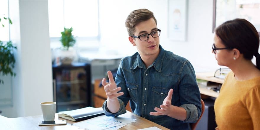 Young man in denim shirt and glasses explaining something to a woman sitting next to him