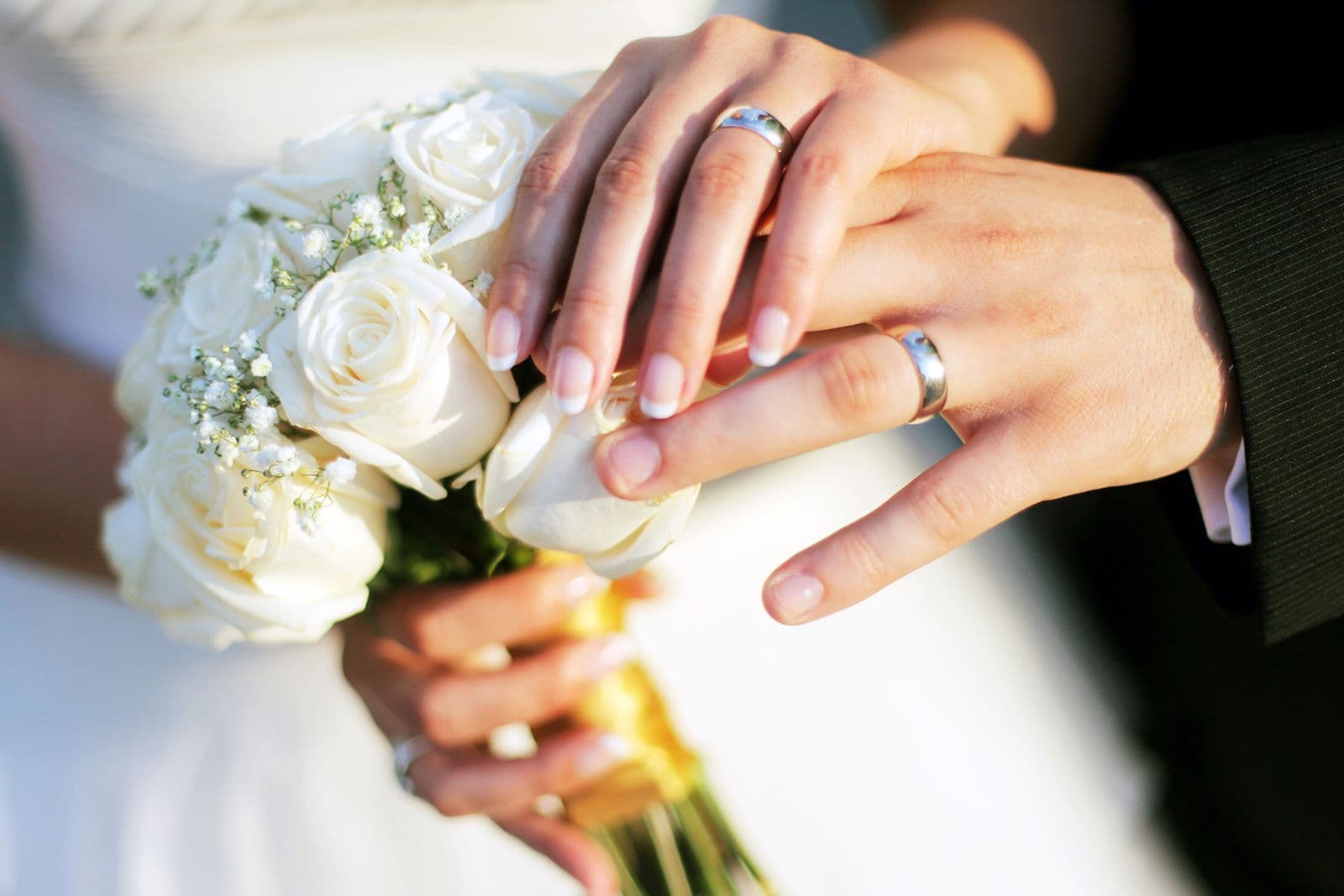 Hands of newly married couple with wedding rings and white flowers
