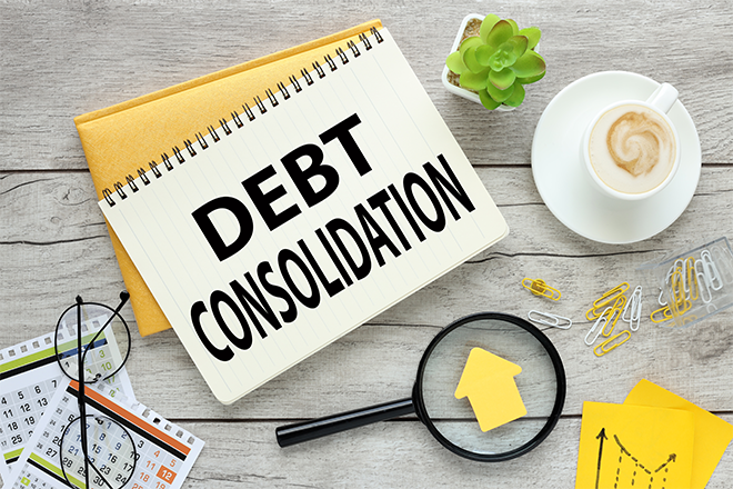 Debt consolidation text written in a notebook laying on the table next to cup of coffee, magnifier and calendars