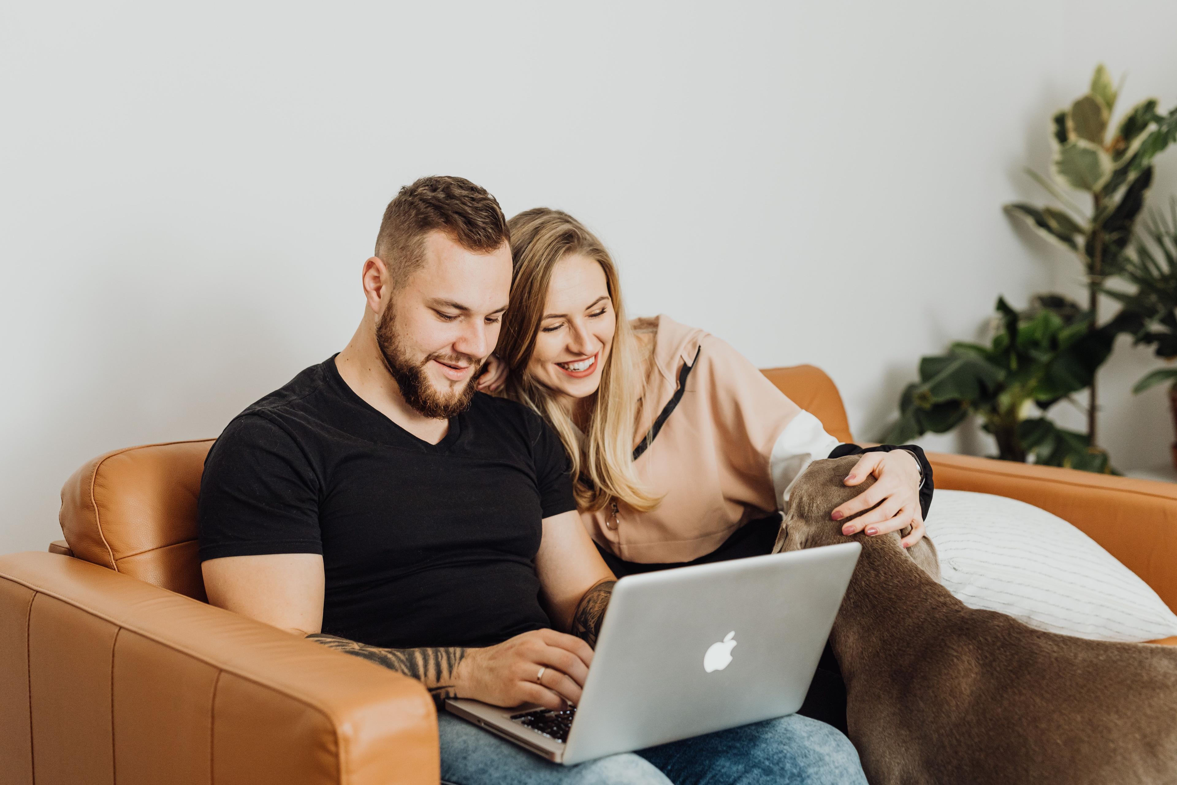 Couple sitting on lounge with laptop and dog