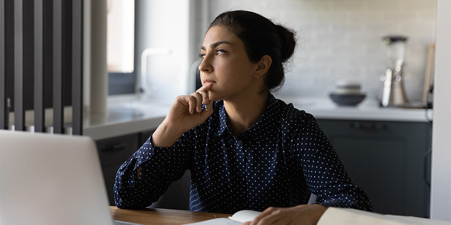 Young woman thinking while sitting with a laptop in front of her