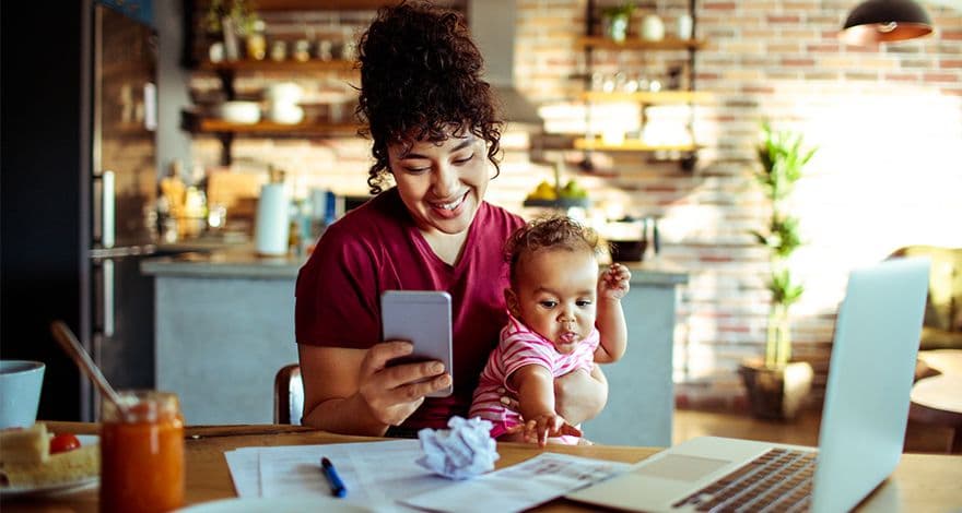 Woman sitting with a baby at a desk, looking on her mobile