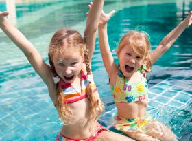 Children in swim suit with hands in the air at the pool