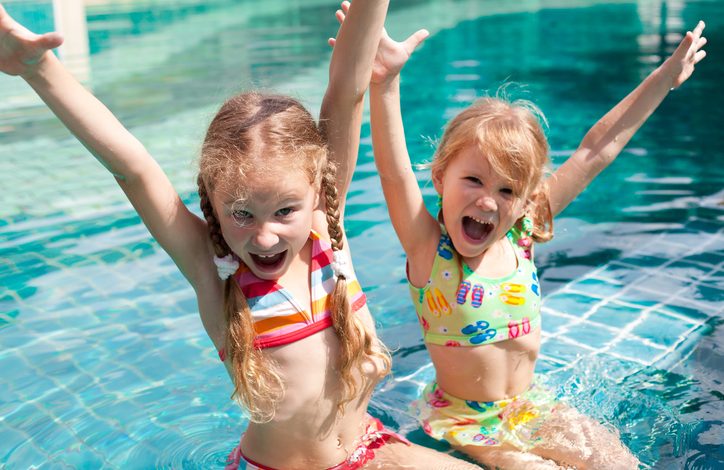 Children in swim suit with hands in the air at the pool