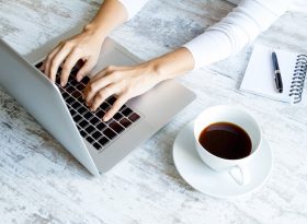 Woman Typing on Laptop with a cup of Coffee