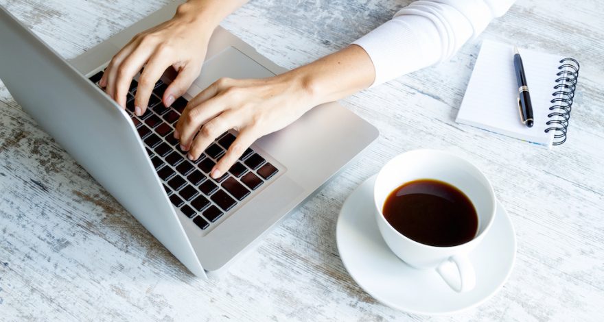 Woman Typing on Laptop with a cup of Coffee