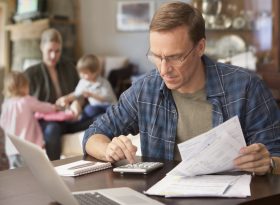 Man in glasses calculating expenses with a calculator