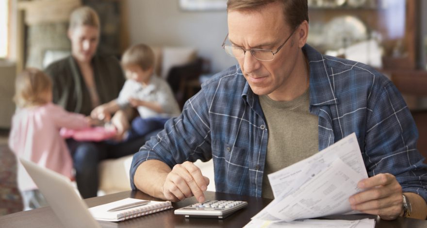 Man in glasses calculating expenses with a calculator