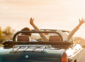 Couple with convertible watching sunset with hands in the air