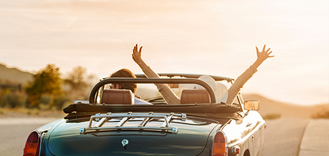 Couple with convertible watching sunset with hands in the air