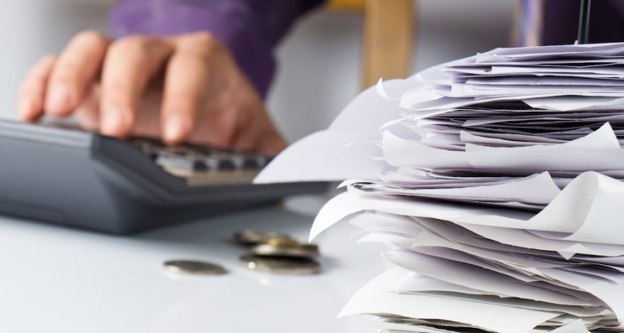 Bills in paper nail with hand calculating | Credit24 Piled up receipts on table