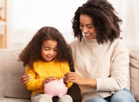 Woman teaching daughter how to save money into piggy bank