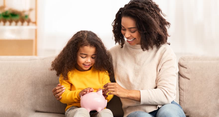 Woman teaching daughter how to save money into piggy bank